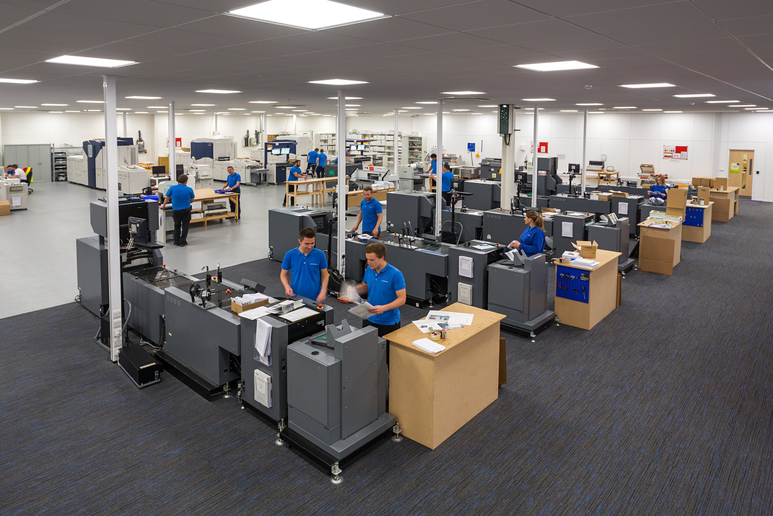 Large electronics manufacturing cleanroom with workers in blue uniforms operating machinery and assembling products.