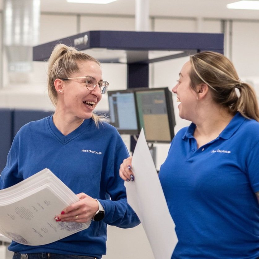 Two women in blue shirts smiling and talking in a workplace.